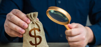 A man examines a dollar money bag through a magnifying glass. Investigating capital origins. Anti money laundering, tax evasion. Study terms and conditions on deposit or loan. Find investments